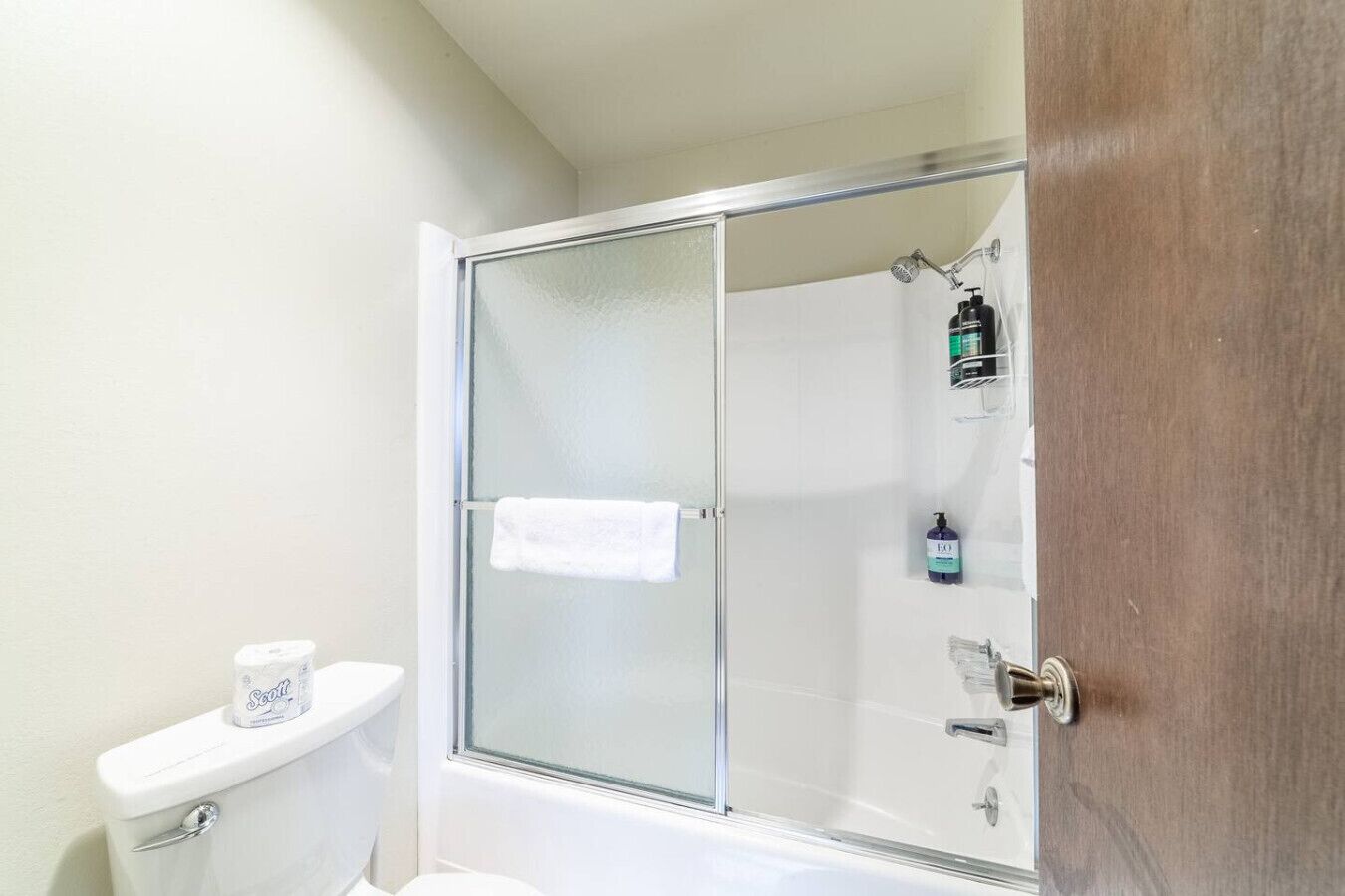A bathroom with a glass-enclosed shower, a toilet, and a towel hanging on the wall.
