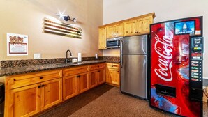 Eine Küche mit Holzausstattung, einem Edelstahlkühlschrank, einer Mikrowelle und einer Coca-Cola-Getränkeautomaten.