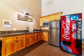A kitchen with wooden cabinets, a stainless steel refrigerator, a microwave, and a Coca-Cola vending machine.