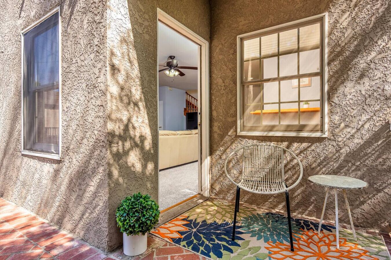 A cozy outdoor area with a textured wall, a small table, a chair, and a colorful rug.