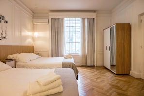 Een hotelkamer met twee bedden, een kledingkast, een raam met gordijnen en een houten vloer.