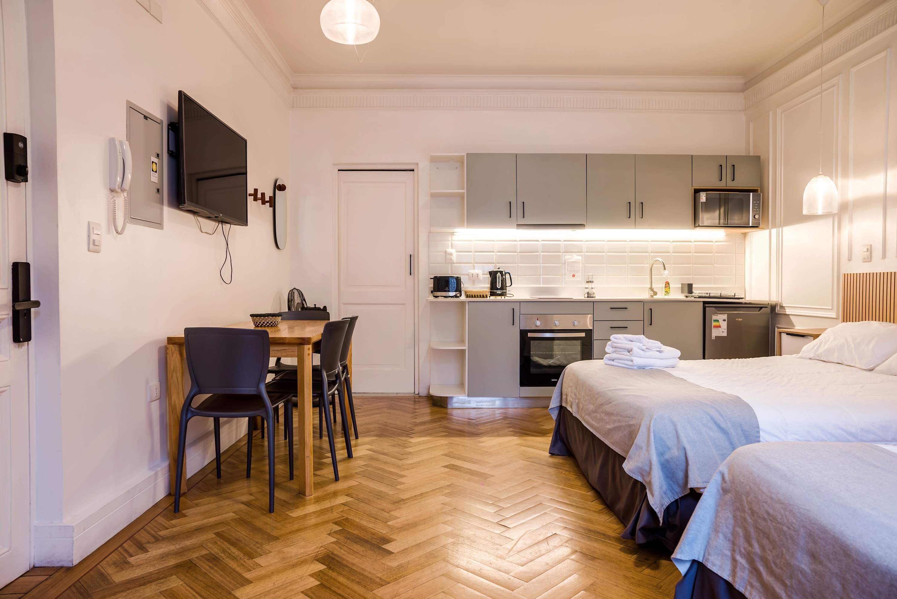 A compact hotel room with a kitchenette, a dining area, and two beds.