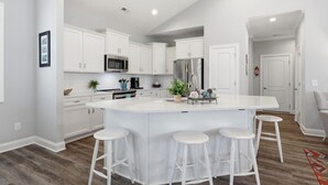 Una cocina moderna con armarios blancos, una isla central con taburetes, electrodomésticos de acero inoxidable y piso de madera.