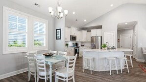 Una cocina moderna con armarios blancos, una isla central con taburetes y un comedor con una mesa redonda y sillas.