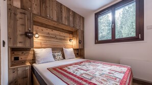 A bedroom with a wooden headboard, a large window, and a quilted bedspread. - Modern Apartment in Courchevel 1850 (Courchevel)