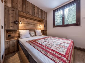 A bedroom with a wooden headboard, a large window, and a quilted bedspread. - Modern Apartment in Courchevel 1850 (Courchevel)