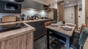 A modern kitchen with a wooden countertop, a black range hood, and a dining area with a table set for four. - Modern Apartment in Courchevel 1850 (Courchevel)