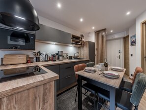 A modern kitchen with a wooden countertop, a black range hood, and a dining area with a table set for four. - Modern Apartment in Courchevel 1850 (Courchevel)
