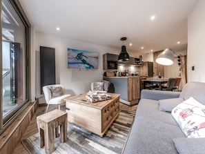 A modern living room with a sofa, a coffee table, and a TV. There is a kitchen area with a dining table and chairs. - Modern Apartment in Courchevel 1850 (Courchevel)