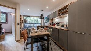 A modern kitchen with a dining area, featuring a wooden table, chairs, and a large window overlooking a deck. - Modern Apartment in Courchevel 1850 (Courchevel)
