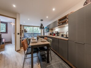 A modern kitchen with a dining area, featuring a wooden table, chairs, and a large window overlooking a deck. - Modern Apartment in Courchevel 1850 (Courchevel)