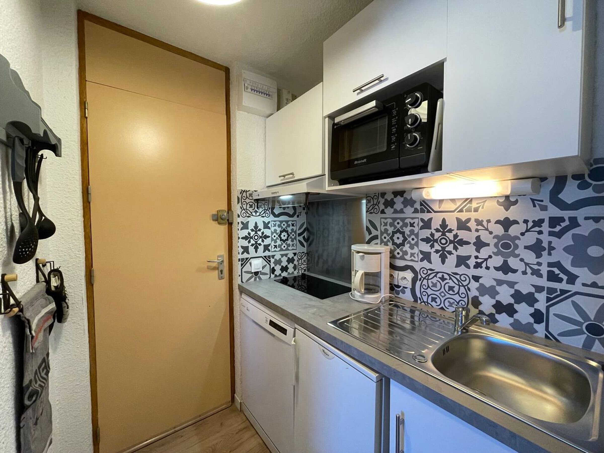 A compact kitchen with a microwave, coffee maker, and stainless steel sink.