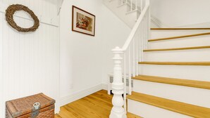 Eine Treppe mit weißen Balustraden und Holzstufen, ein Korbwesen und ein gerahmtes Bild an der Wand.