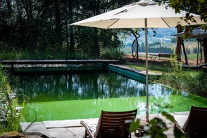 A serene outdoor pool area with a wooden deck, a lounge chair, and a table under a canopy. - Renovated apartment just 20 km from Florence in the Tuscan hills (Scandicci)