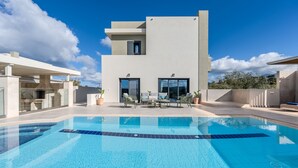 Ein modernes Haus mit Swimmingpool, Gartenmöbeln und blauem Himmel.
