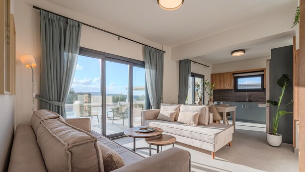 Ein modernes Wohnzimmer mit Sofa, Couchtisch und Ausblick auf den Himmel durch große Fenster.