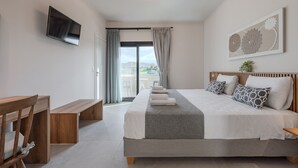 Ein modernes Schlafzimmer mit einem großen Bett, einem Flachbildfernseher, einer hölzernen Bank und Blick ins Freie.