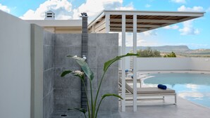 Un área de piscina moderna al aire libre con un muro de piedra, una silla de descanso y una pérgola.