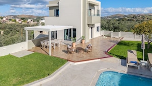 Una casa moderna de dos pisos con un patio, mobiliario exterior y una piscina.