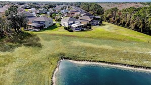 Vista aerea di una zona residenziale con case, un ampio prato e un corpo d'acqua.