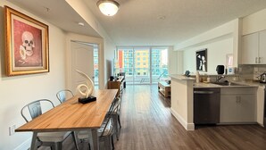 Une cuisine moderne avec une table à manger en bois, des chaises et une vue sur un balcon donnant sur des immeubles.