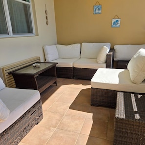 Un espace extérieur lumineux, aménagé avec des meubles en osier et une table à plateau en verre.