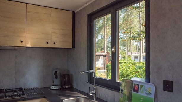 Eine moderne Küche mit einem großen Fenster, einem Gasherd, einer Spüle und einem Schneidebrett.