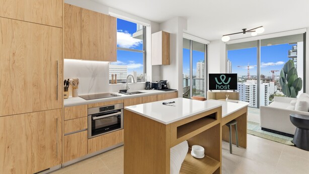 A modern kitchen with wooden cabinets, a white countertop, and a city view through large windows. - City Views Downtown Miami (Miami)