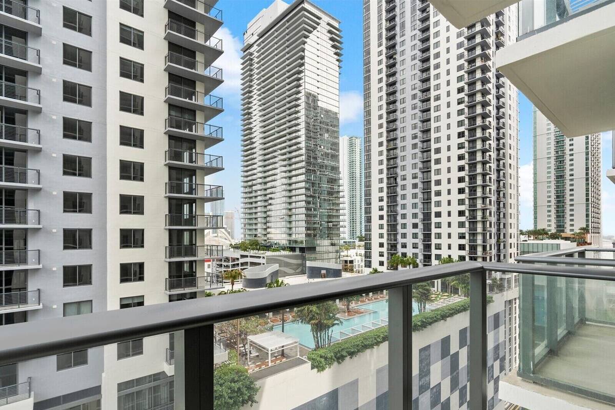 Um edifício residencial alto com várias varandas, uma piscina no terraço e vista para edifícios altos ao redor.