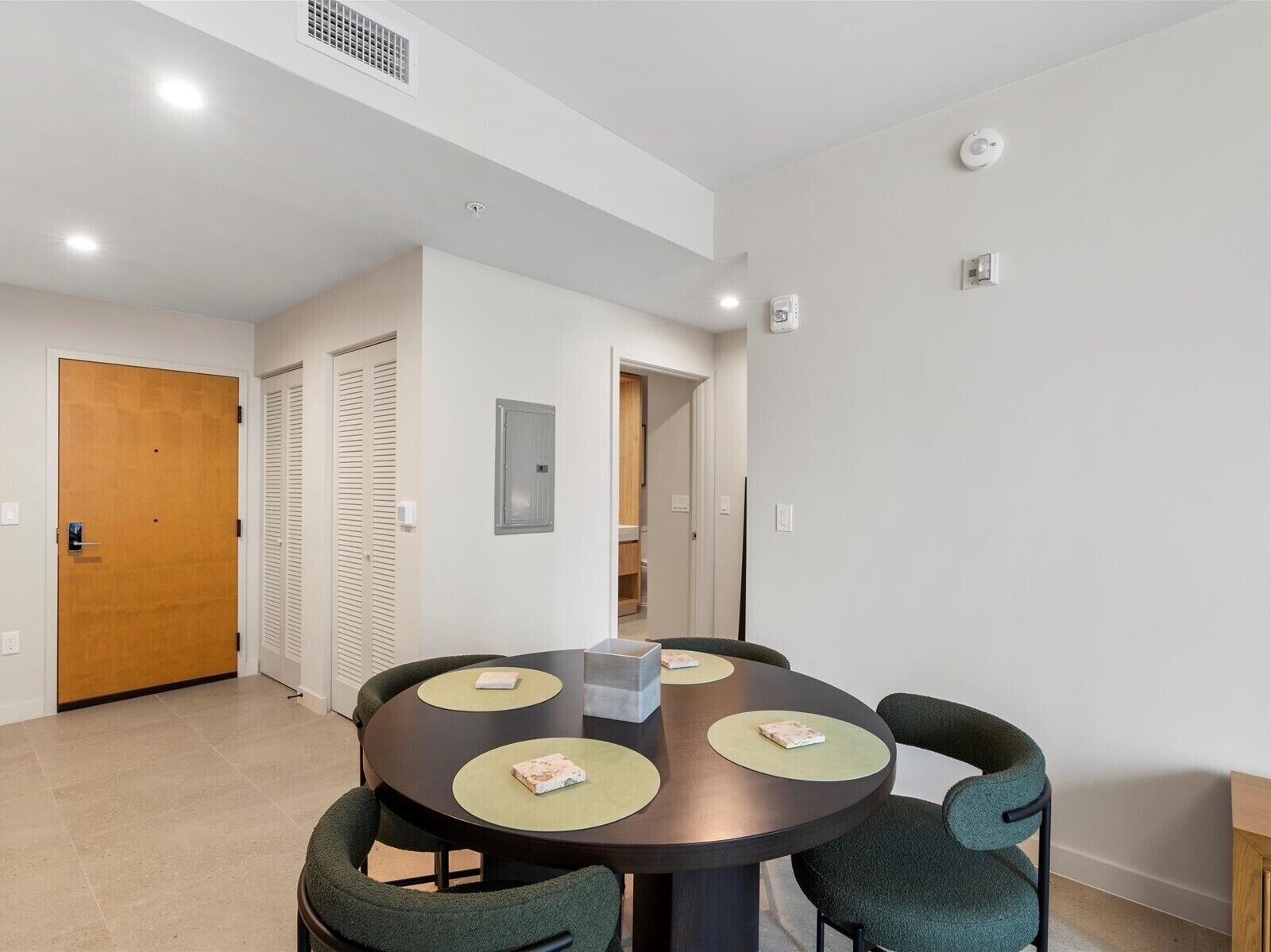 A modern dining area with a round table, four chairs, and a wooden door in the background.