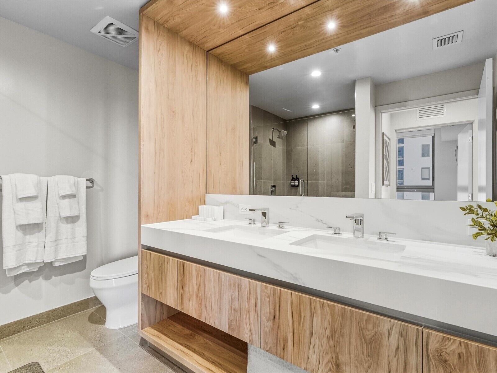 Un baño moderno con tocador de madera, un espejo grande y zona de ducha.