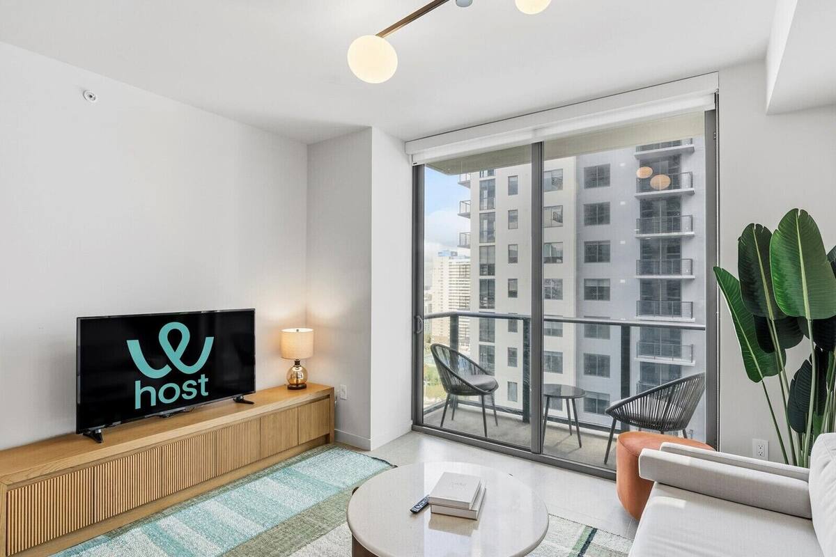 Uma sala de estar moderna com televisão, sofá, mesa de centro e uma varanda com vista para a cidade.