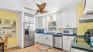 Cocina con armarios blancos, un refrigerador de acero inoxidable, un microondas y un ventilador de techo.