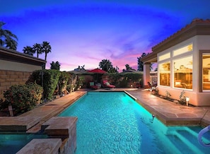 A swimming pool with a patio area, surrounded by a landscaped garden and a building with large windows. - Gorgeous house with private pool/hot tub in a gated community in Bermuda Dunes. (Bermuda Dunes)
