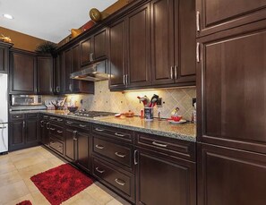 A kitchen with dark wooden cabinets, a granite countertop, and a red rug. - Gorgeous house with private pool/hot tub in a gated community in Bermuda Dunes. (Bermuda Dunes)