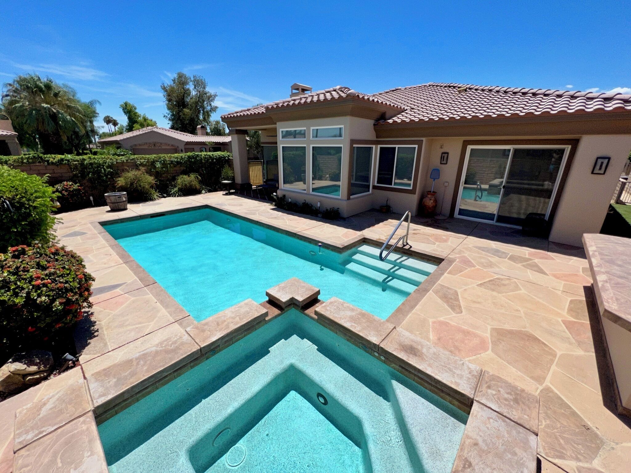 A rectangular swimming pool with a diving board, surrounded by stone tiles and a small deck area.