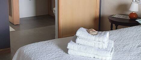 Quarto de hotel com cama, banheiro com espelho e mesa de cabeceira com abajur.