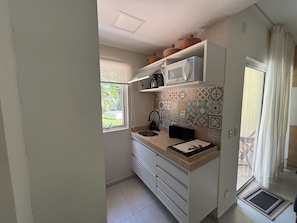 A compact kitchen with a microwave, sink, and patterned backsplash. - Flat Premium Solar Água Apart Hotel - Pipa (Tibau do Sul)