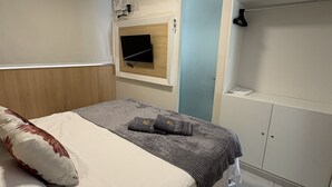 Un dormitorio con cama, televisor montado en la pared, armario y una puerta.