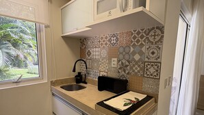 Una cocina con pileta, encimera y alacenas. Se observa una ventana con vista a follaje.