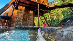 Una estructura de madera con una piscina, rodeada de vegetación.