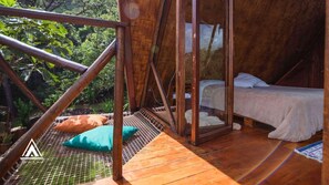 A wooden cabin with a bed, a hammock, and a view of the surrounding forest.