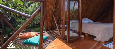A wooden cabin with a bed, a hammock, and a view of the surrounding forest.