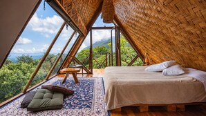 A bedroom with a large window, a bed, a chair, and a rug.