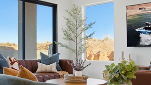 A modern living room with a large window, a brown leather sofa, a round coffee table, and a potted plant. - The Lookout- Luxe, Hot Tub, Firepit, 50-Mile Views (Page)