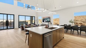 A spacious kitchen with a large island, modern pendant lights, and a view of a desert landscape through large windows. - The Lookout- Luxe, Hot Tub, Firepit, 50-Mile Views (Page)