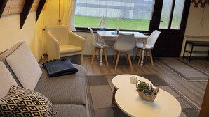 Une pièce chaleureuse avec un plafond en pente, un canapé, une table et une fenêtre donnant sur un jardin.