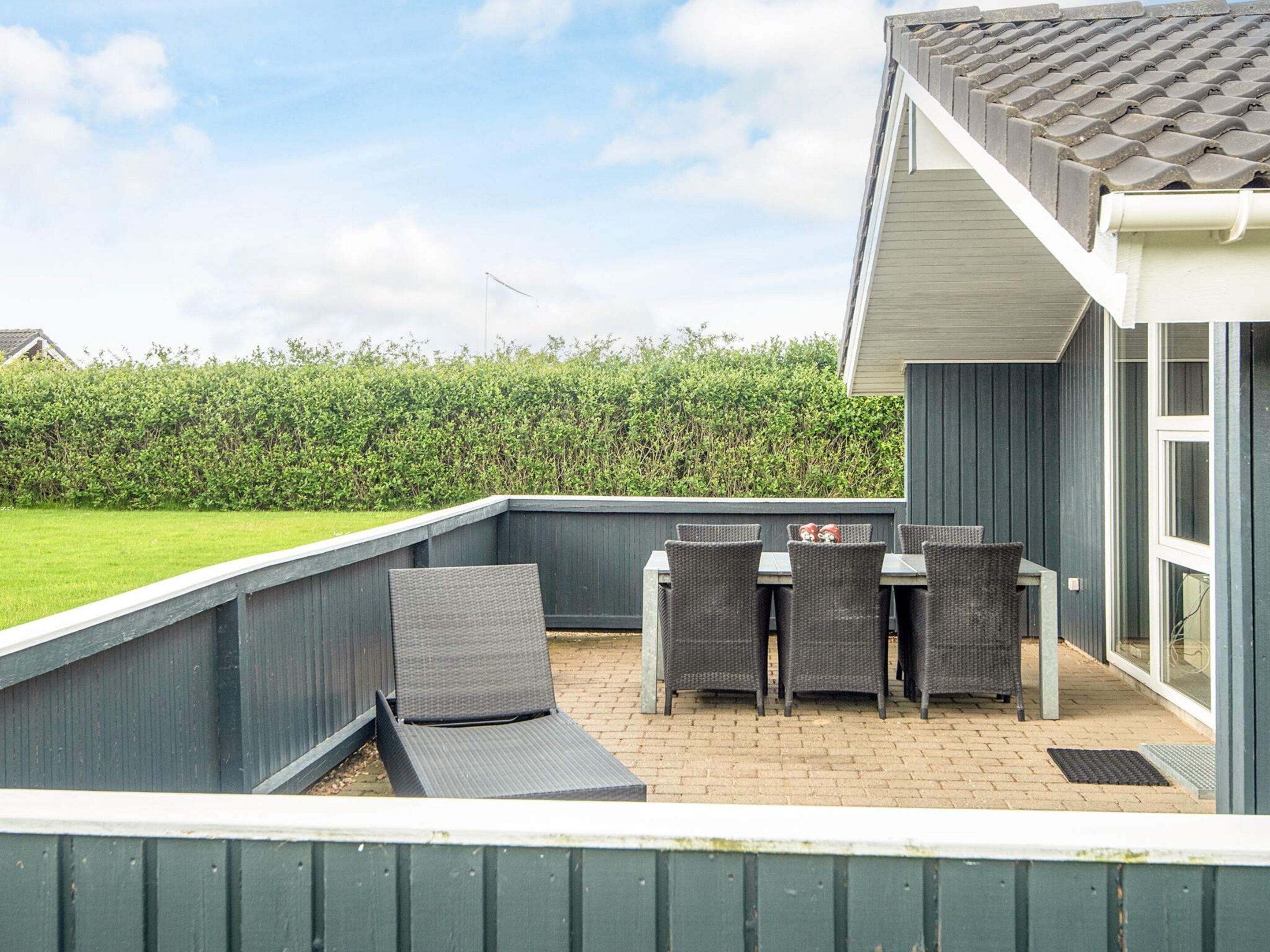 An outdoor patio with a table and chairs, a covered seating area, and a view of a hedge and a building in the background.