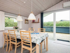 Ein Essbereich mit einem Tisch für vier Personen, Holzsesseln, Pendelleuchten und Blick durch eine Glastür.