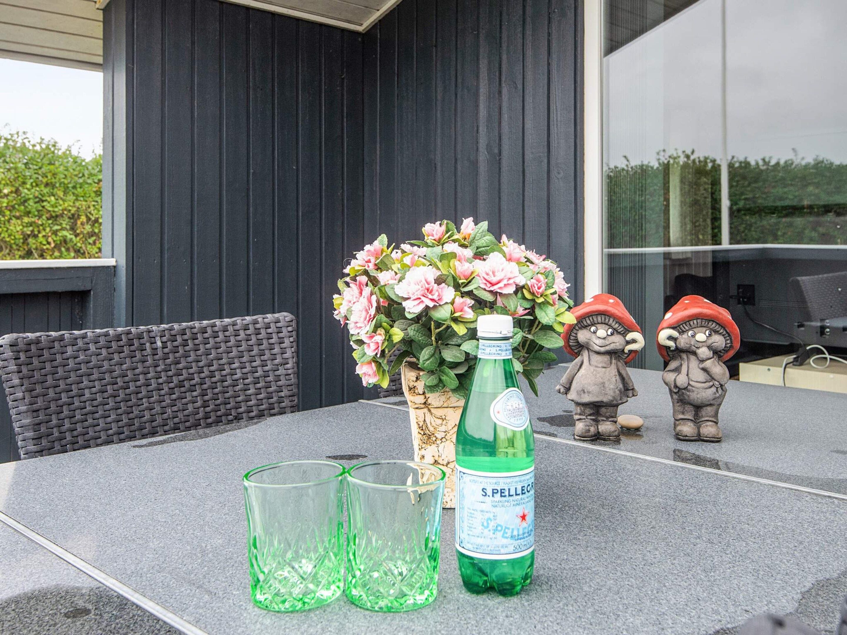 Une table avec deux verres vides, une bouteille d’eau pétillante S.Pellegrini et une plante en pot ornée de fleurs roses.